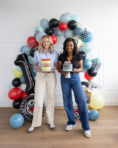 Two women holding their race car decorated cakes in front of the photo booth setup
